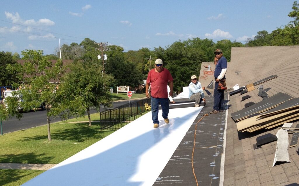 Workers installing white roofing material on a building.