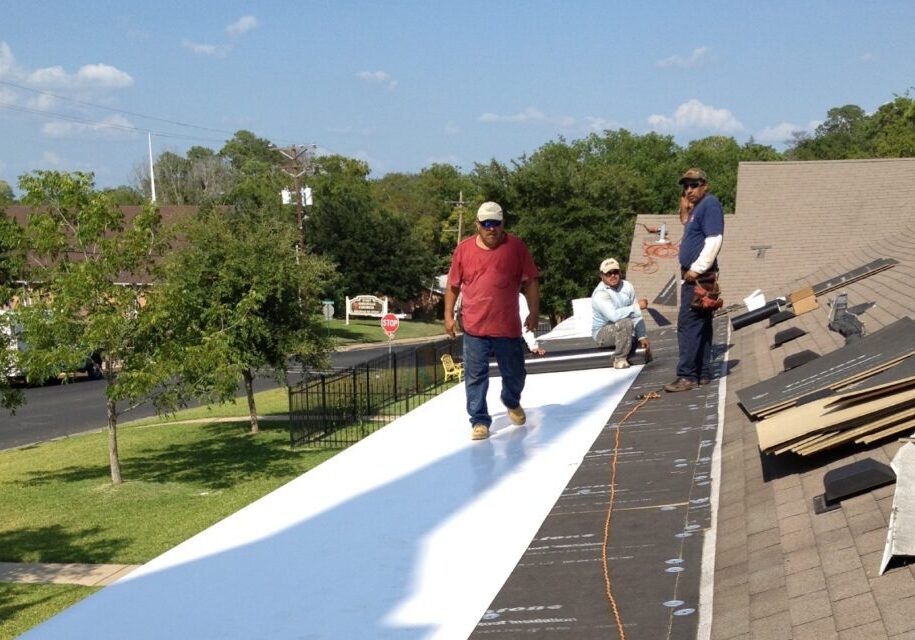 Workers installing white roofing material on a building.